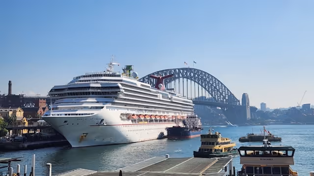 A large cruise ship, the Carnival Splendor, docked at Sydney's Overseas Passenger Terminal with the Harbour Bridge in the background, alongside ferries.