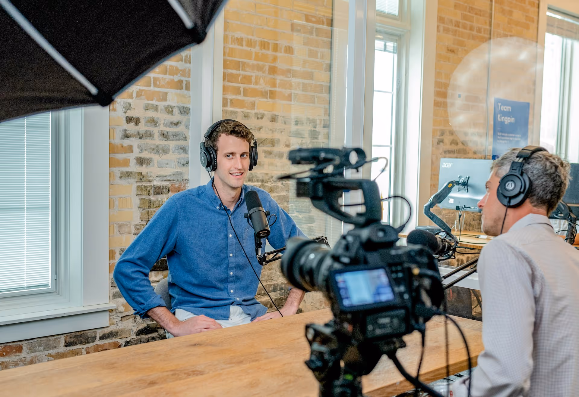 A professional podcast interview setup with a guest wearing headphones and speaking into a microphone, while a cameraman records the conversation.