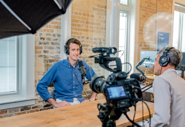 A professional podcast interview setup with a guest wearing headphones and speaking into a microphone, while a cameraman records the conversation.