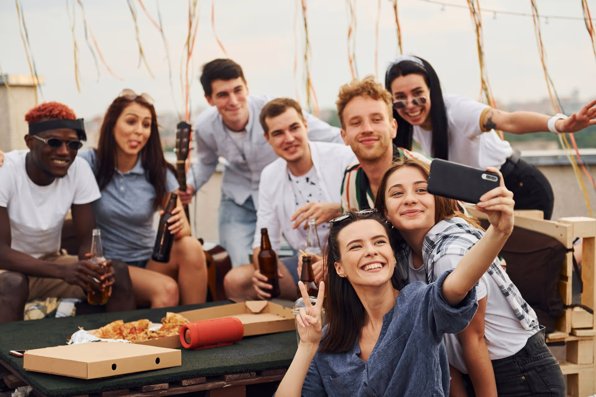 A group of adults enjoying a gathering, smiling and posing for a selfie with streamers hanging in the background.
