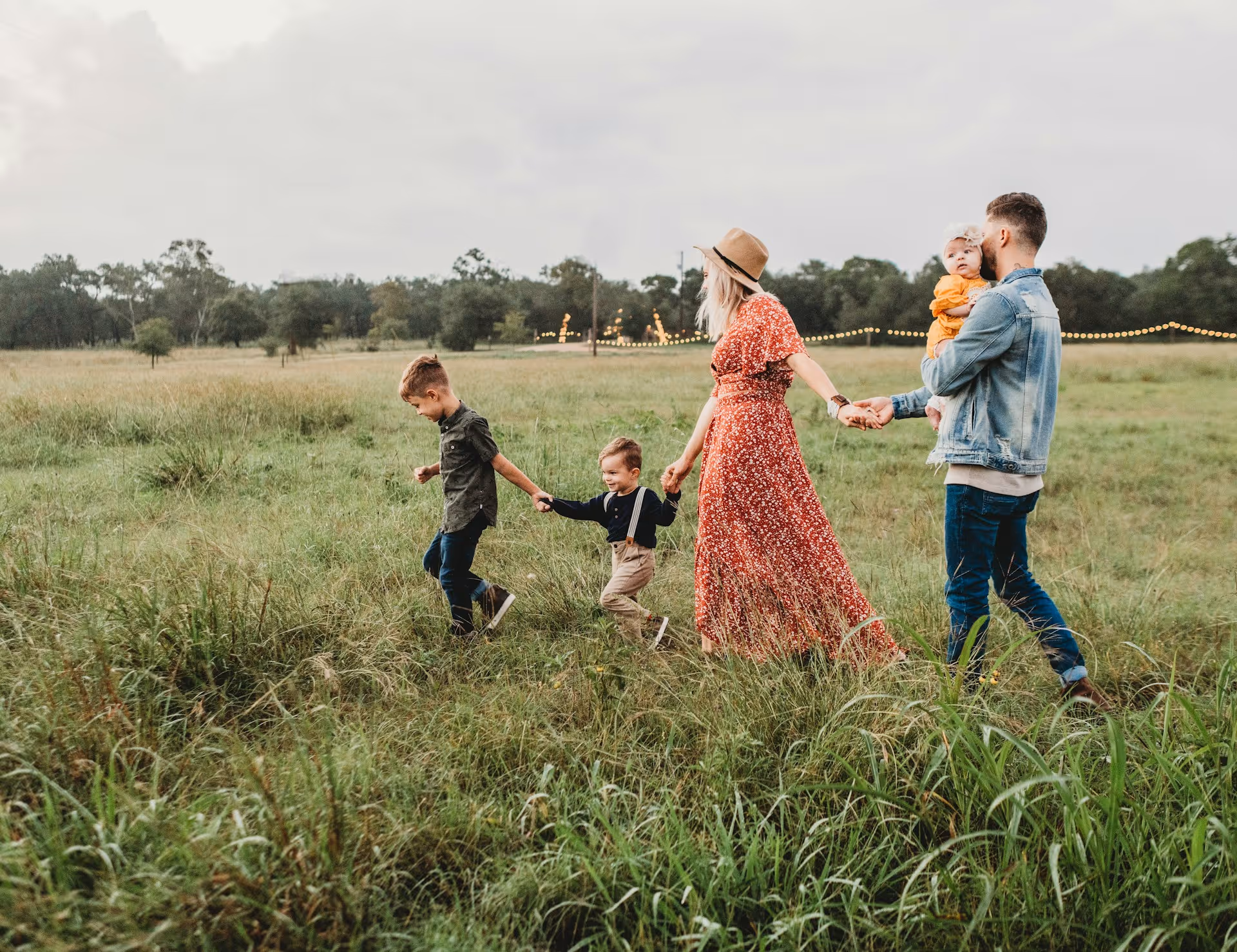 A family with young children walking hand in hand through a grassy field, enjoying quality time outdoors during a holiday.