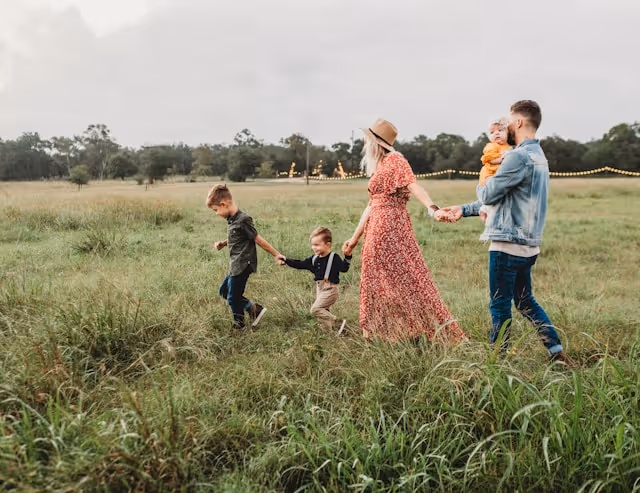 A family with young children walking hand in hand through a grassy field, enjoying quality time outdoors during a holiday.