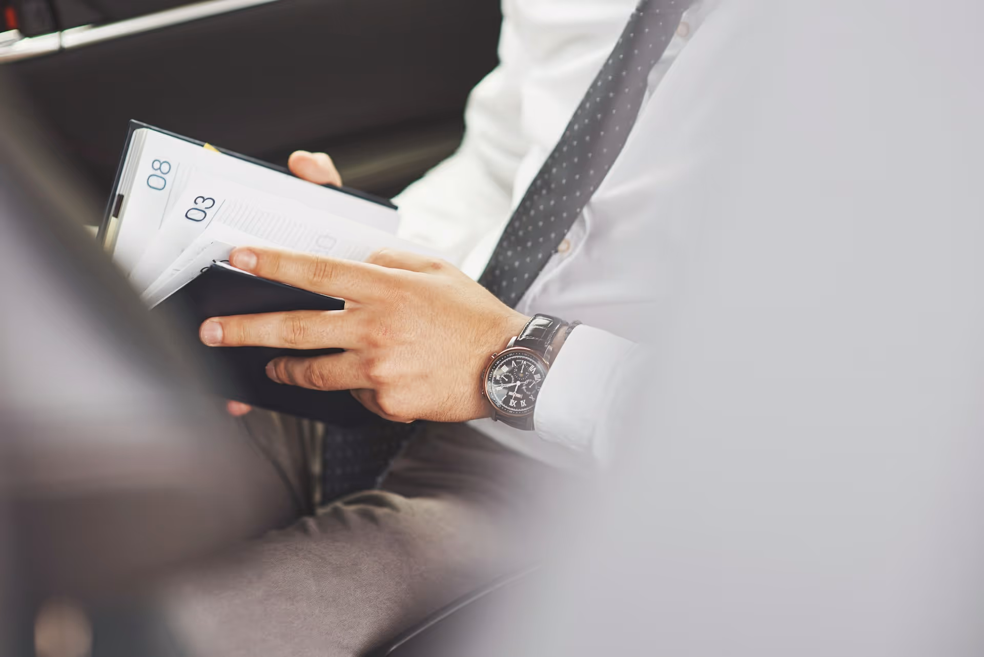 Business professional reviewing a planner while seated in the back of a chauffeured car.