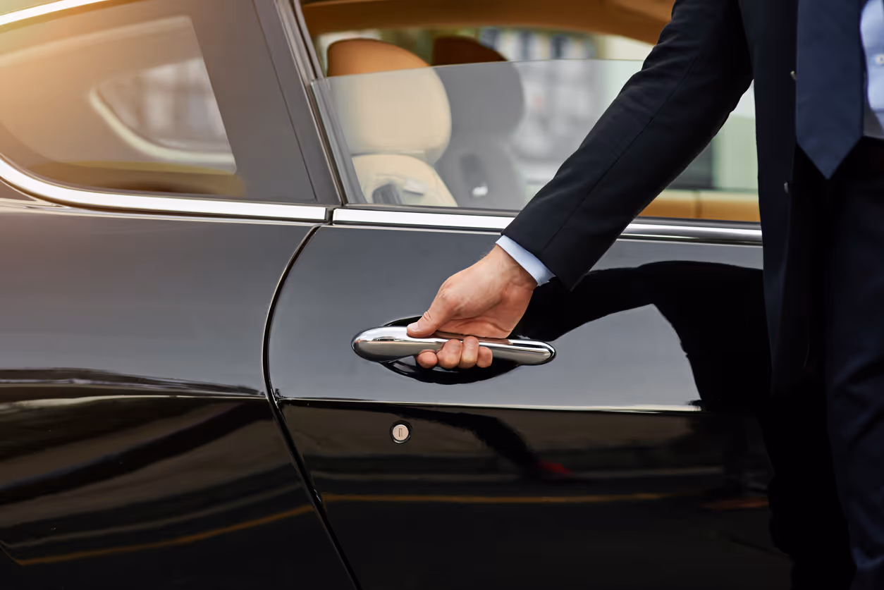 Chauffeur in a dark suit opening the rear door of a premium black vehicle, with a professional and polished appearance.