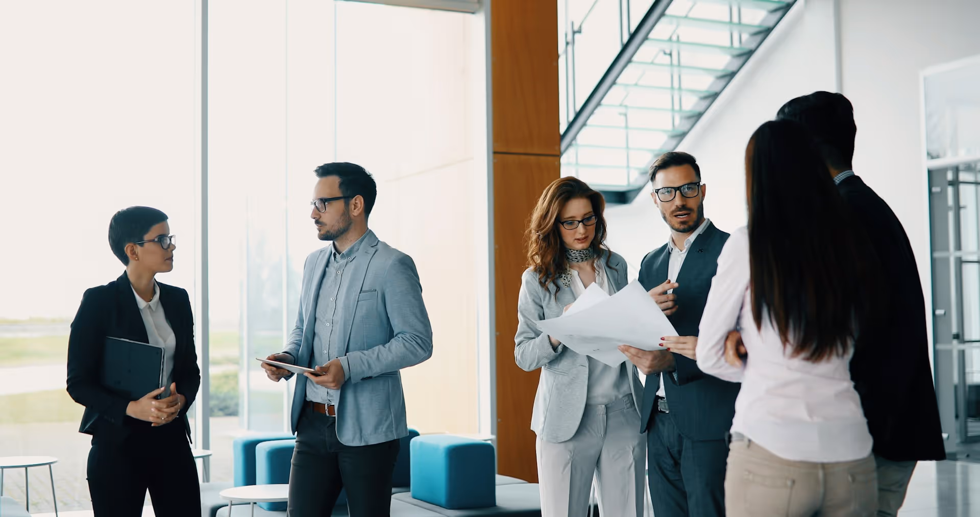 A group of professionally dressed colleagues stands in a bright and modern office space.