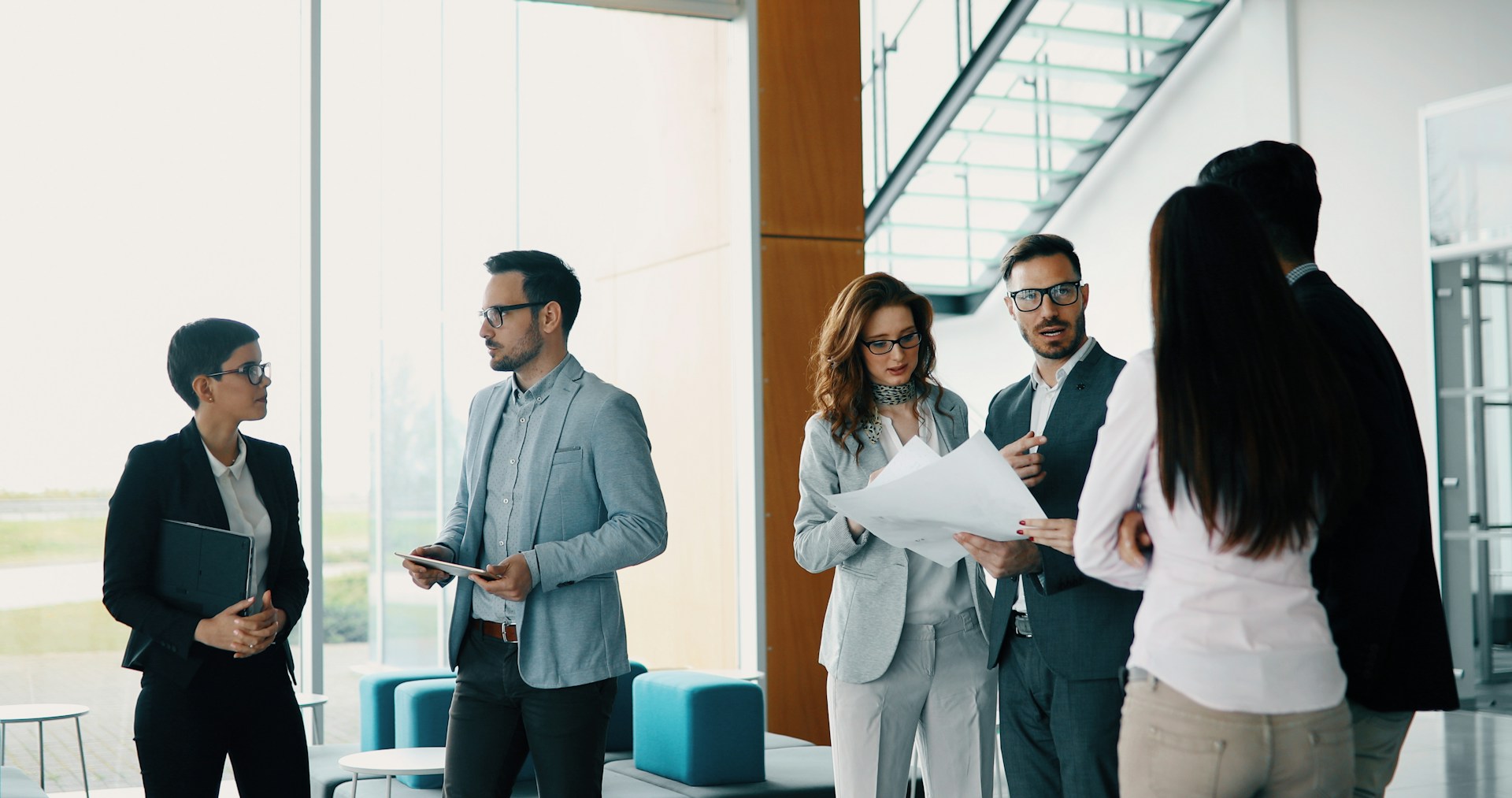 A group of professionally dressed colleagues stands in a bright and modern office space.