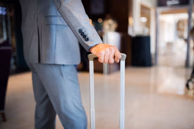 Close-up of a business traveller in a grey suit holding a suitcase handle, symbolising modern corporate travel with a focus on comfort, professionalism and seamless transitions.