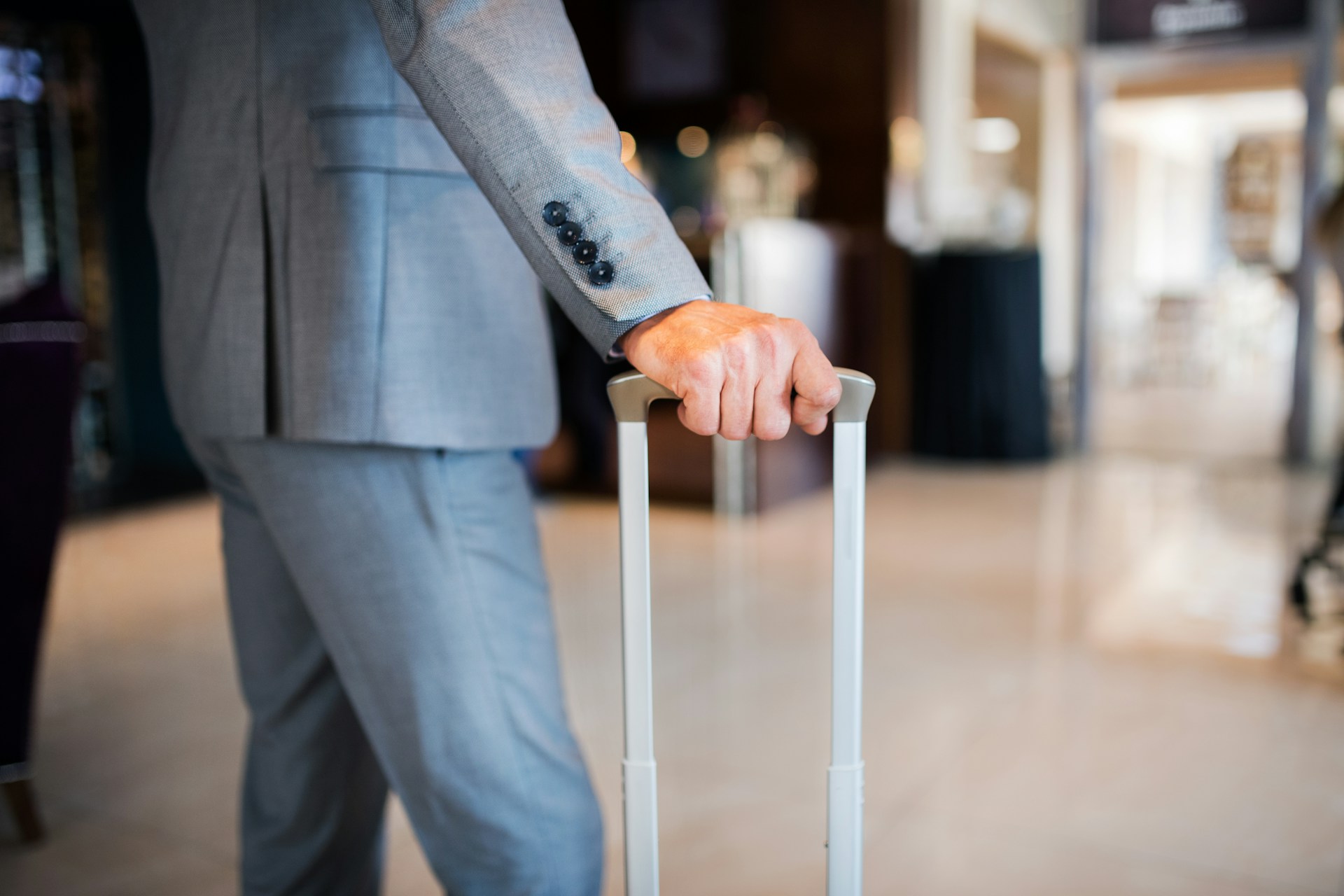 Close-up of a business traveller in a grey suit holding a suitcase handle, symbolising modern corporate travel with a focus on comfort, professionalism and seamless transitions.