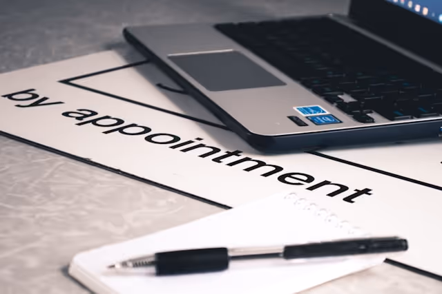 Close-up of a sign reading "by appointment" alongside a laptop and notepad, representing scheduled commitments and the convenience of having a chauffeur wait during appointments or events.