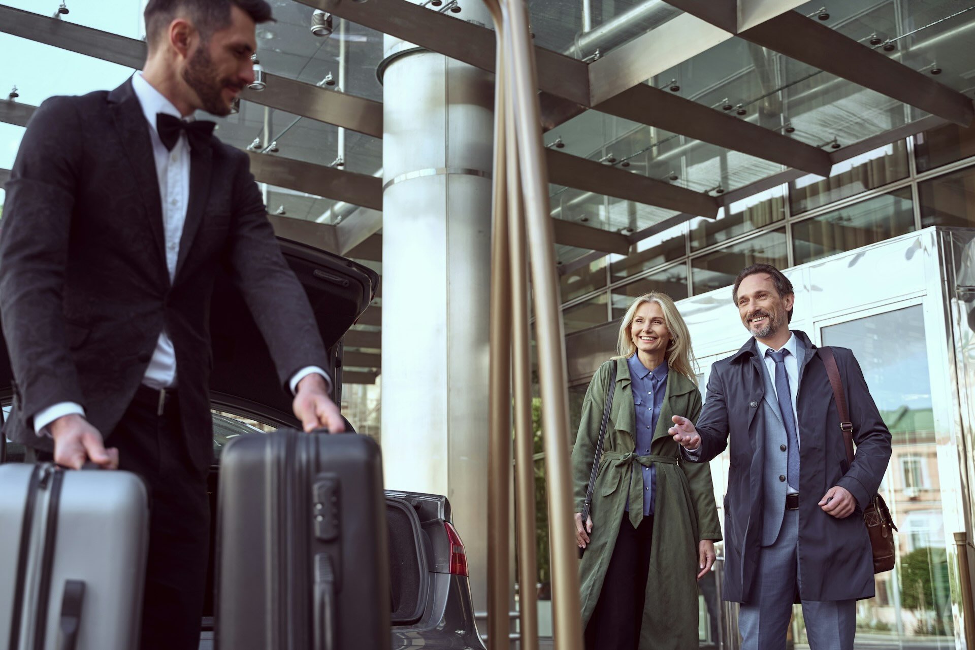 Chauffeur assisting hotel guests with luggage at the entrance of a hotel, representing seamless and professional ground transport arranged by concierge services.