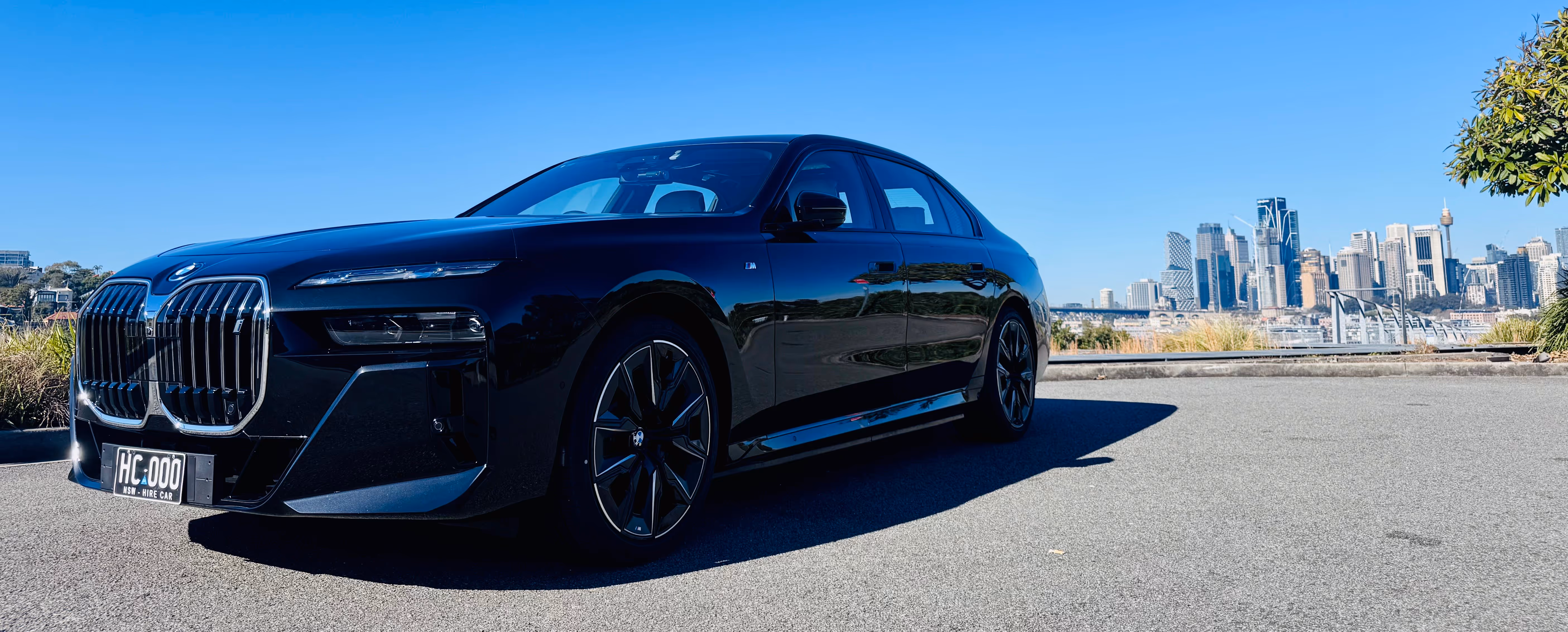 Evoke's black BMW i7 parked with Sydney’s skyline in the background under a clear blue sky.