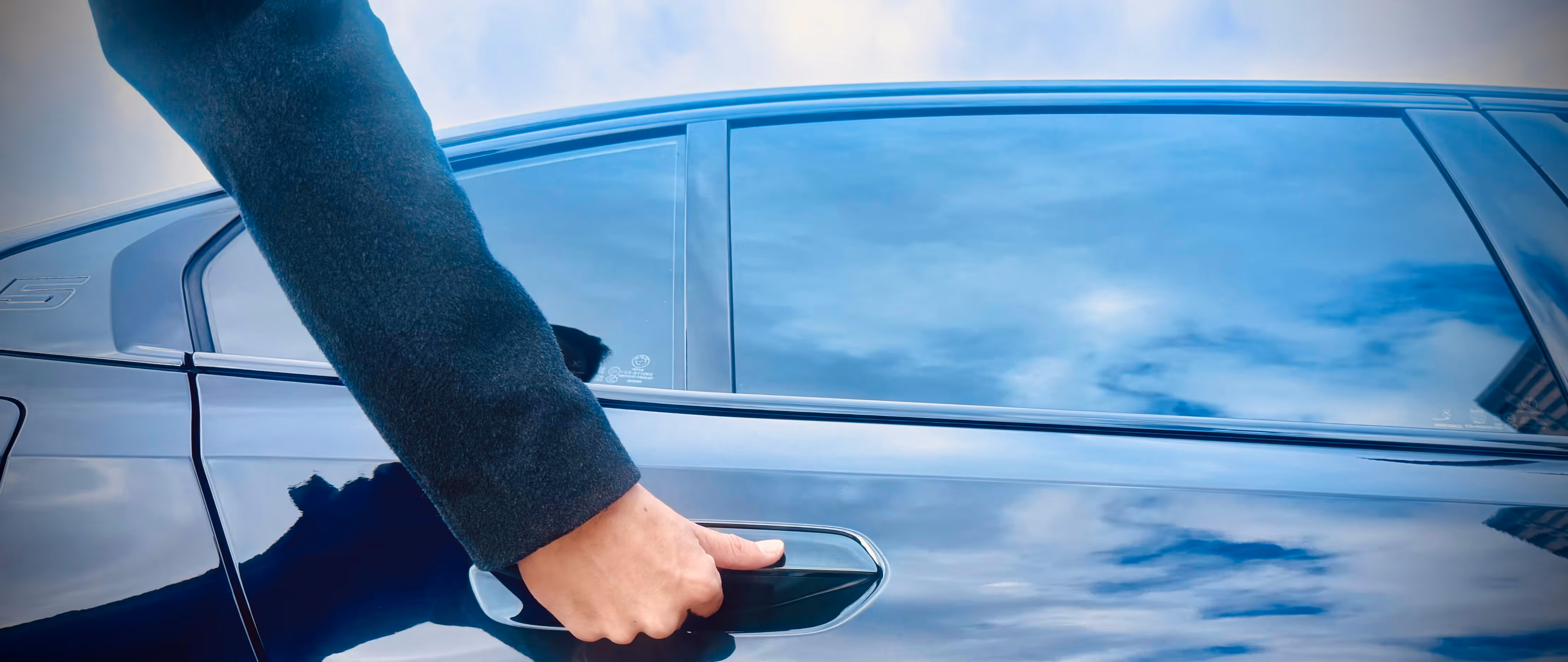 Chauffeur opening the door of a polished hire car, reflecting the sky, symbolising professional chauffeured hire car service with premium attention to detail.