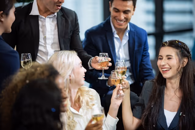 A group of professionally dressed colleagues celebrating with drinks at an end-of-year corporate event.