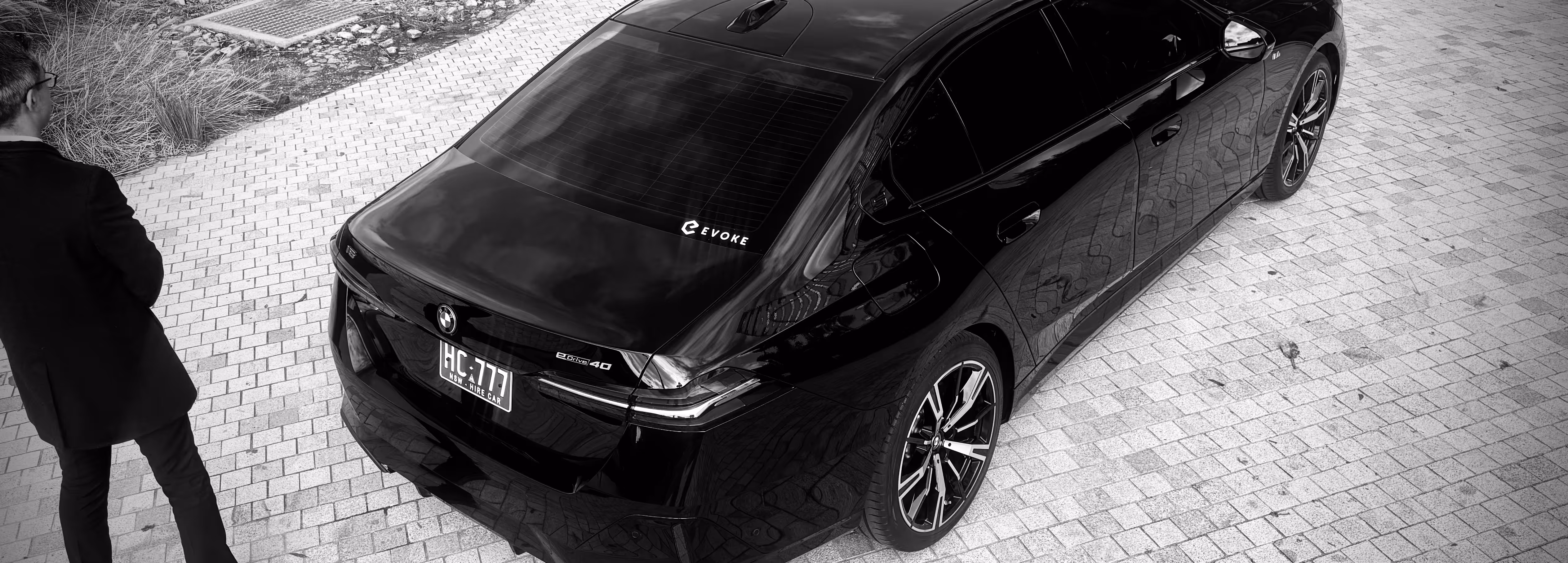 Chauffeur standing behind a black BMW with Evoke branding, viewed from above.