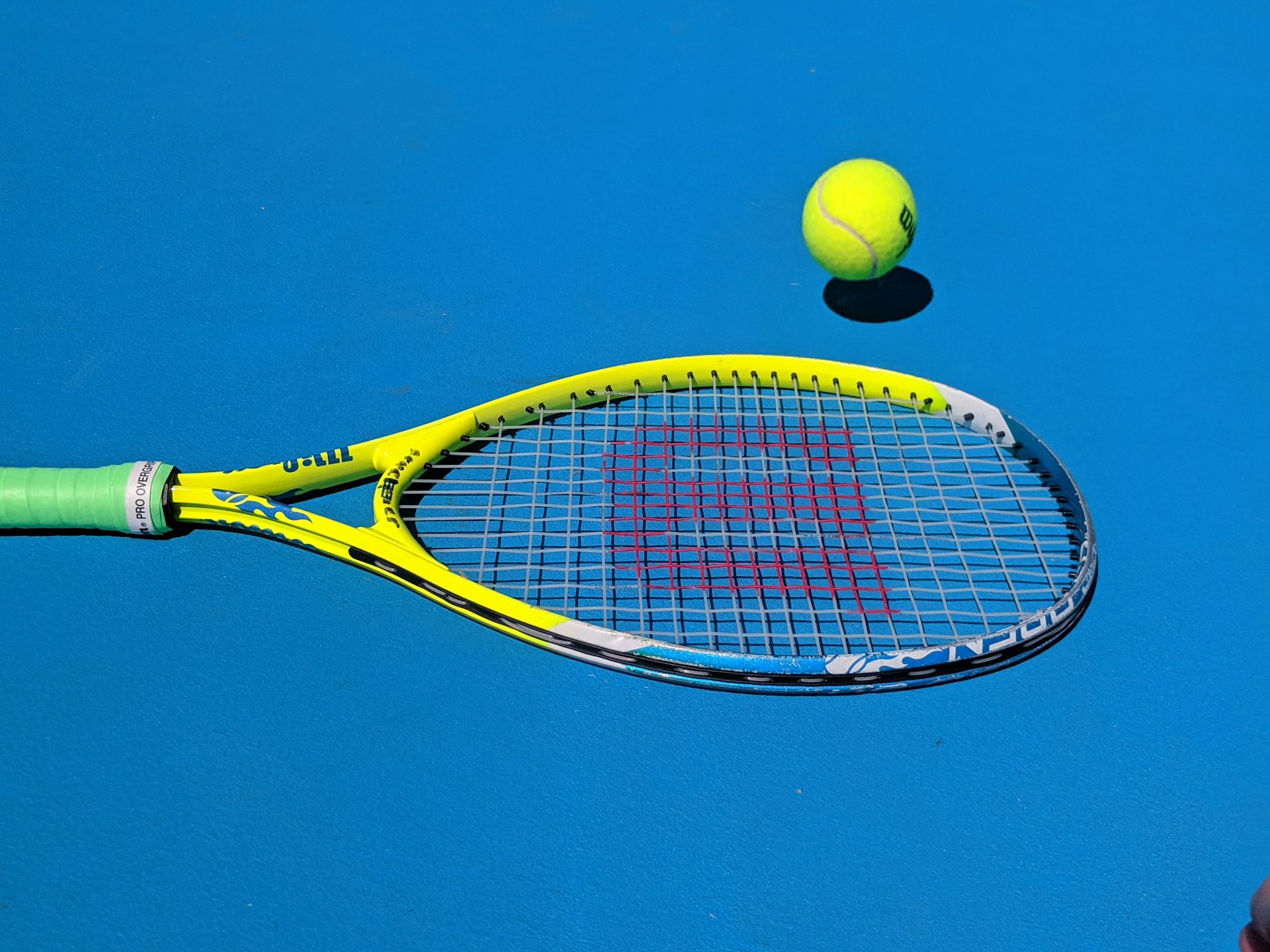 Close-up of a tennis racket and ball on a bright blue court.