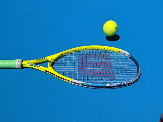 Close-up of a tennis racket and ball on a bright blue court.