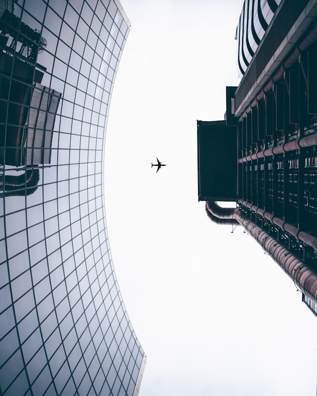 Plane flying overhead between city buildings, symbolising business travel, airport transfers and flexible chauffeur support across Australian cities.