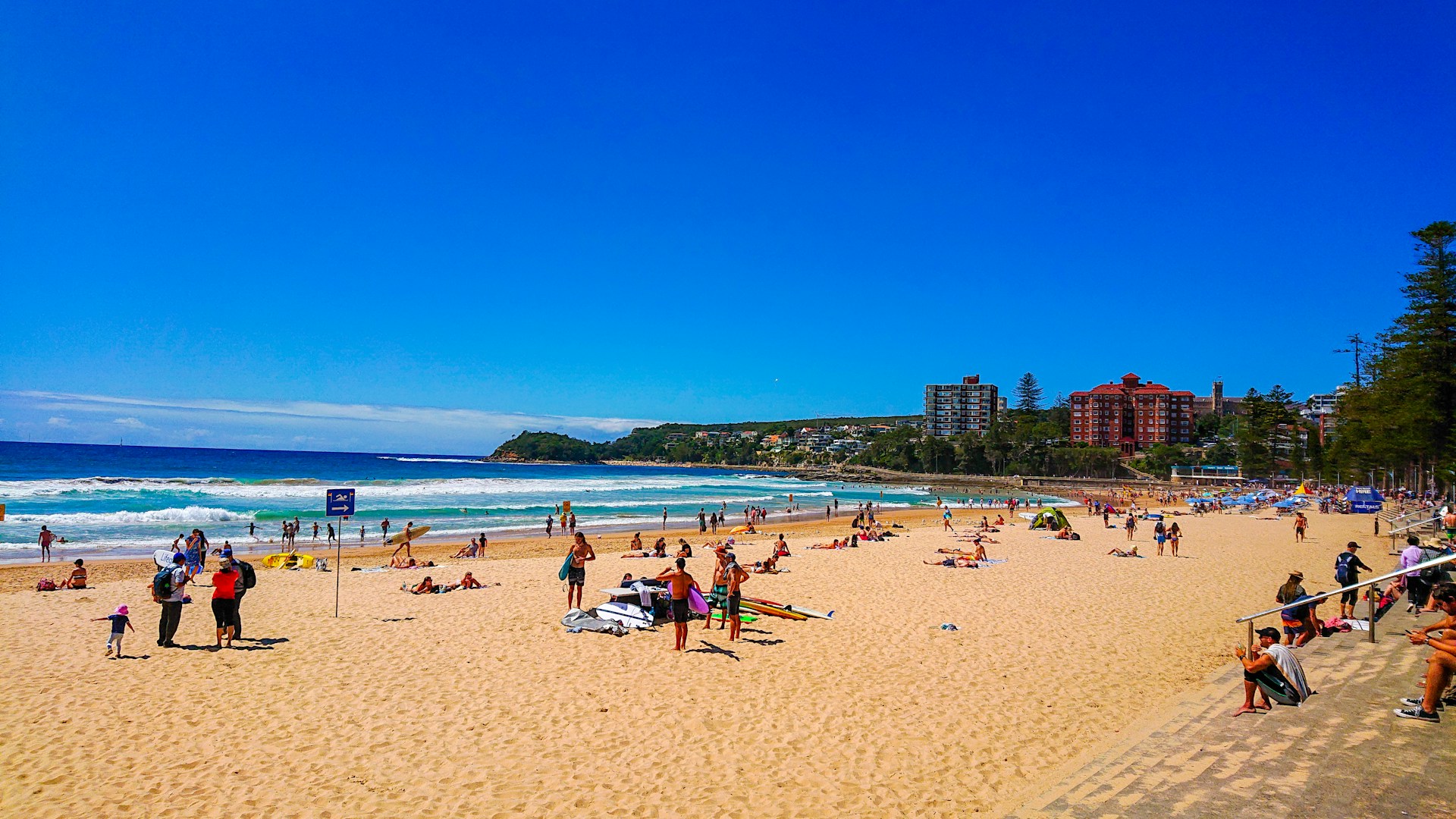 People enjoying Manly Beach on a sunny day with ocean views and the Manly coastline in Sydney.