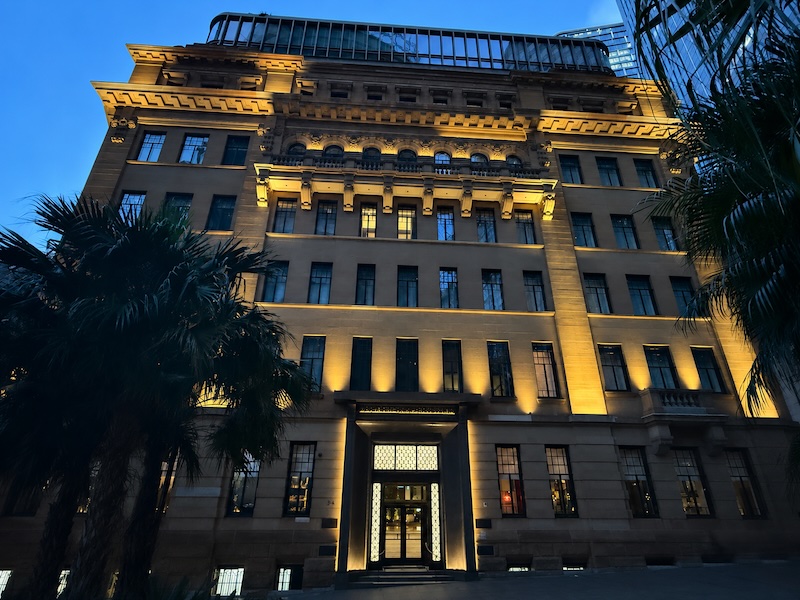 Illuminated façade of Capella Sydney at dusk, showcasing its heritage sandstone architecture.