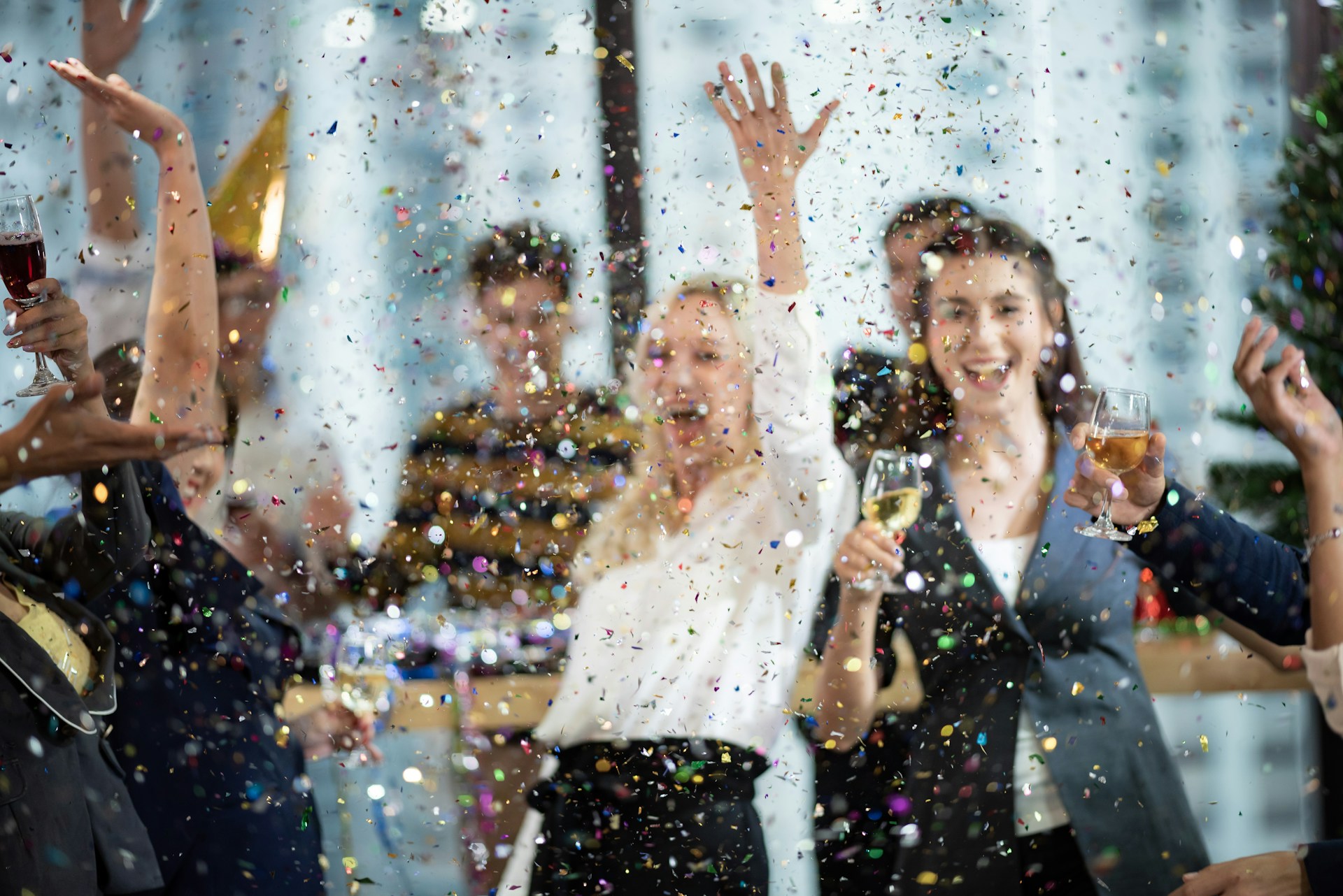 A group of coworkers celebrating indoors, raising glasses as colourful confetti falls around them.