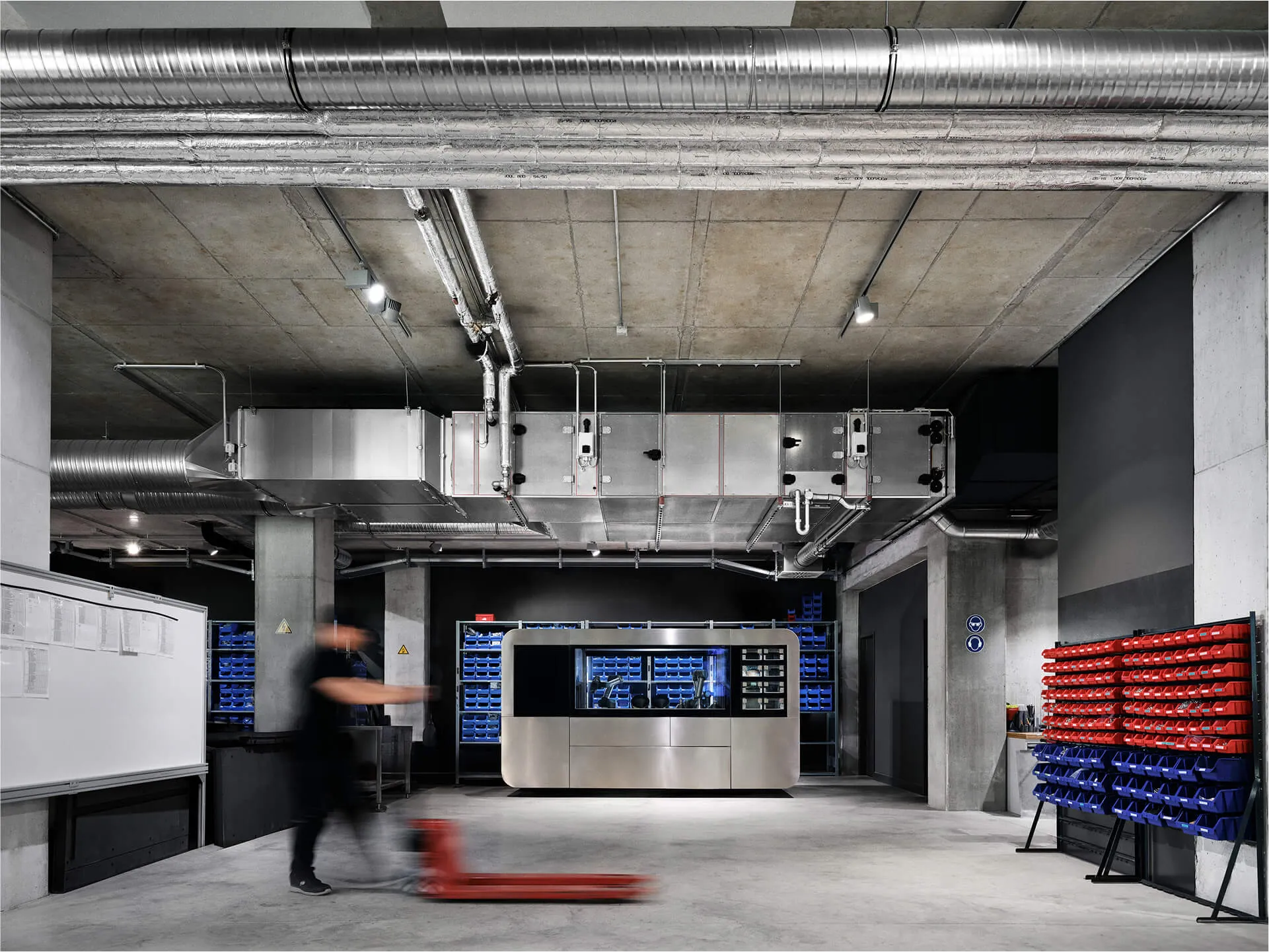 CA product unit in an industrial lab setting with exposed pipes, storage bins, and a worker moving equipment in the foreground.