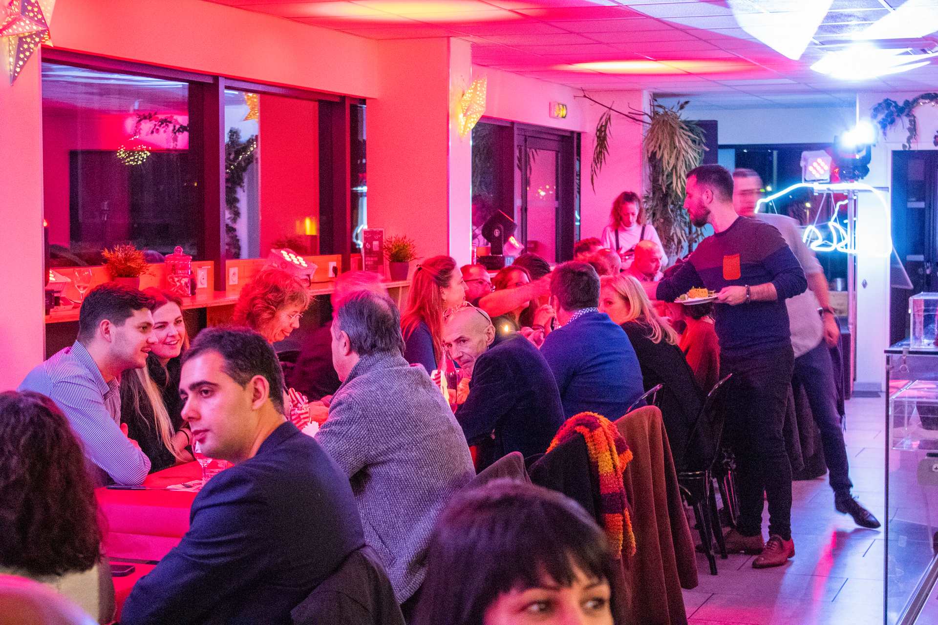 Soirée Prestige 2022 à Montpellier : convives installés à la grande tablée, discussion animée sous lumière rouge.