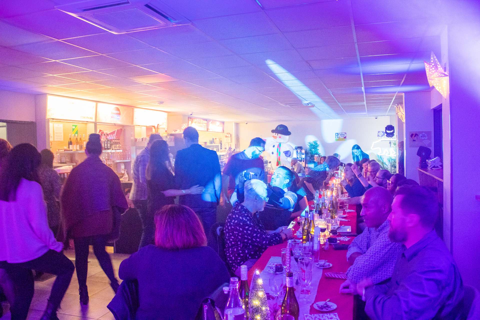 Soirée Prestige 2022 à Montpellier : invités rassemblés près du couloir et du bar, lumière bleue, décor de fin d'année.