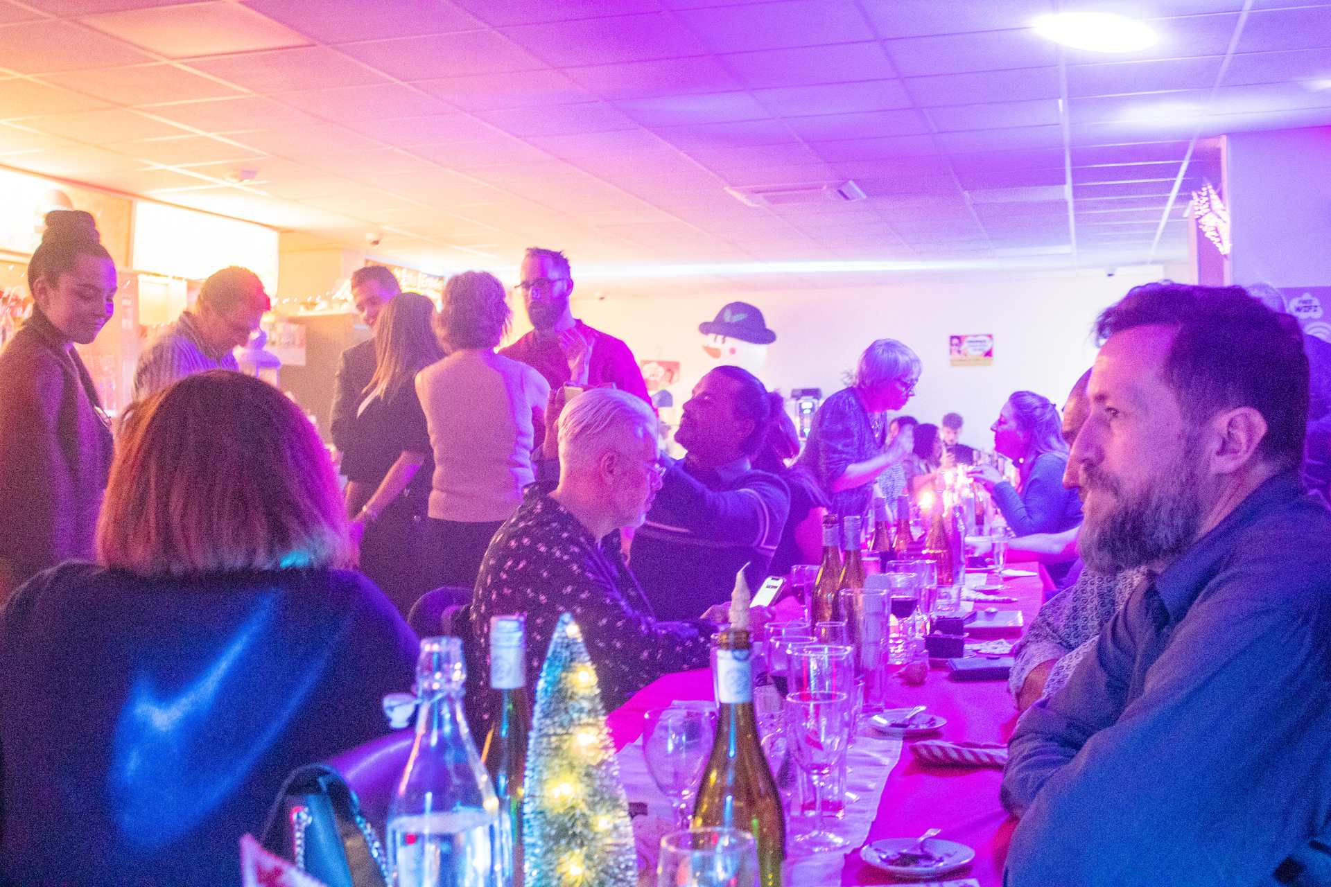 Soirée Prestige 2022 à Montpellier : convives à table sous éclairage violet, sapin de Noël en arrière-plan.