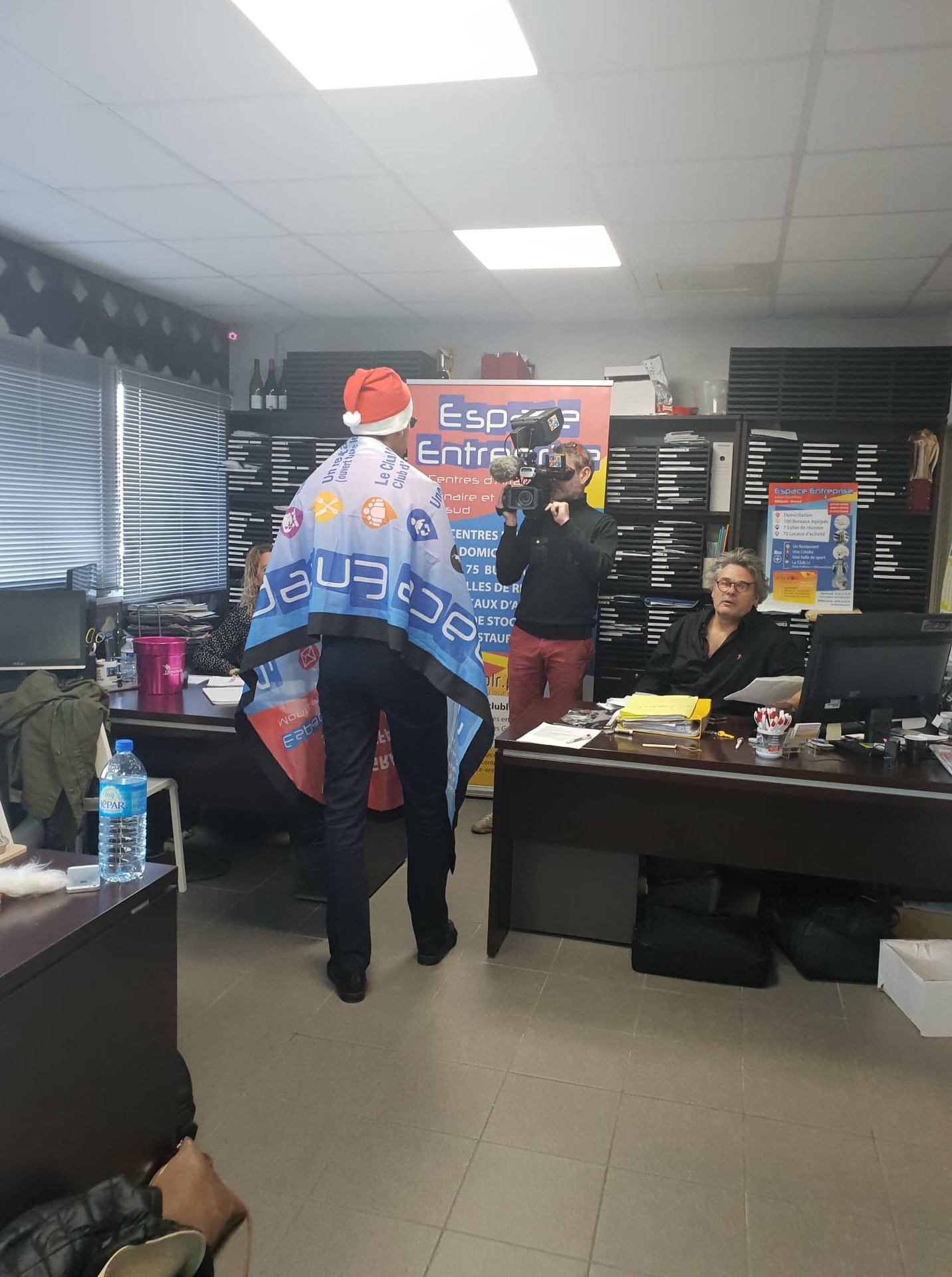 Vœux 2019 Espace Entreprise à Montpellier : collaborateur en bonnet de Père Noël drapé dans la banderole Espace Entreprise, filmé de dos par l'équipe de tournage.