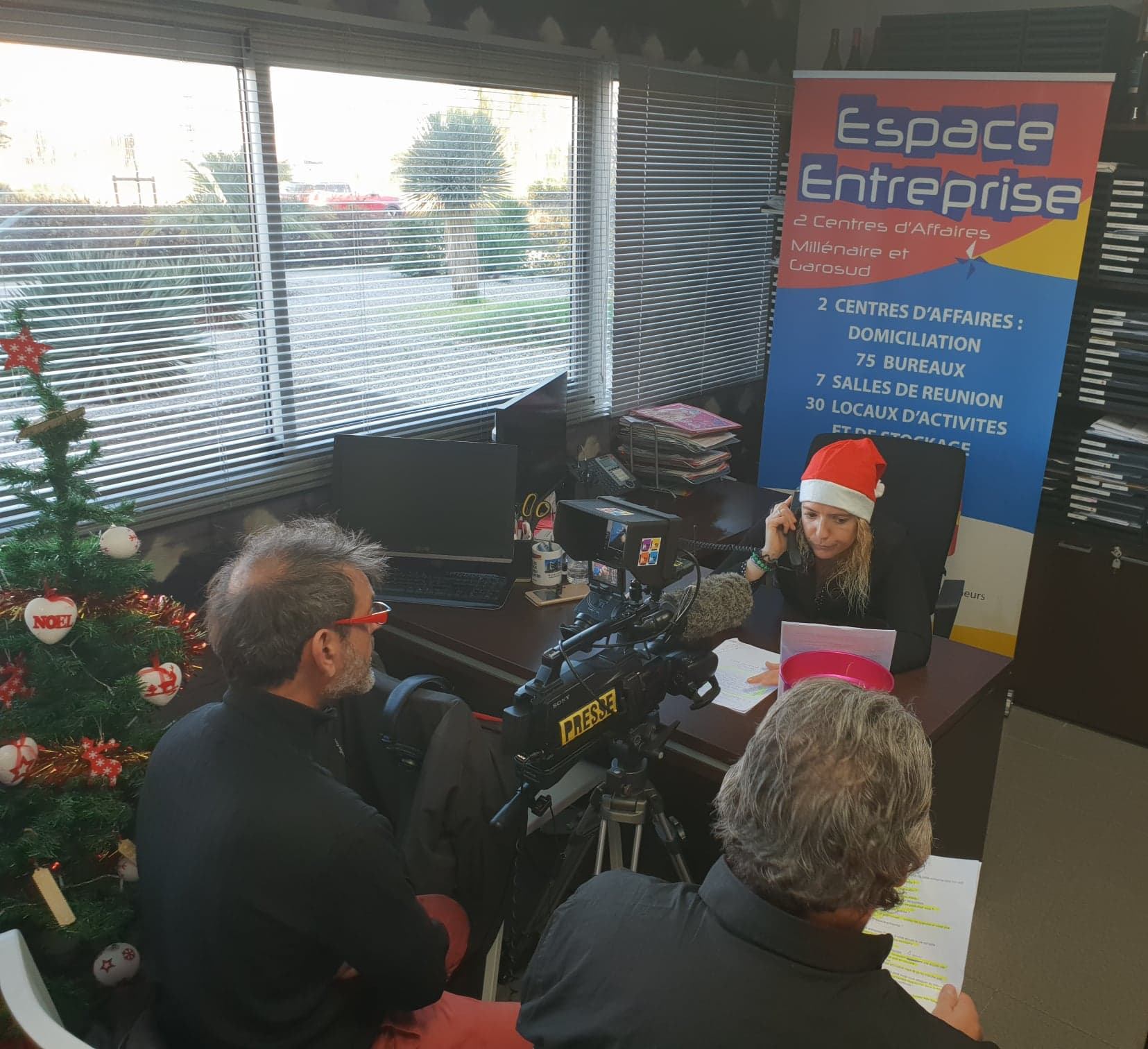 Vœux 2019 Espace Entreprise à Montpellier : équipe de tournage (caméra et perche son) filmant une collaboratrice en bonnet de Père Noël, sapin de Noël en arrière-plan.