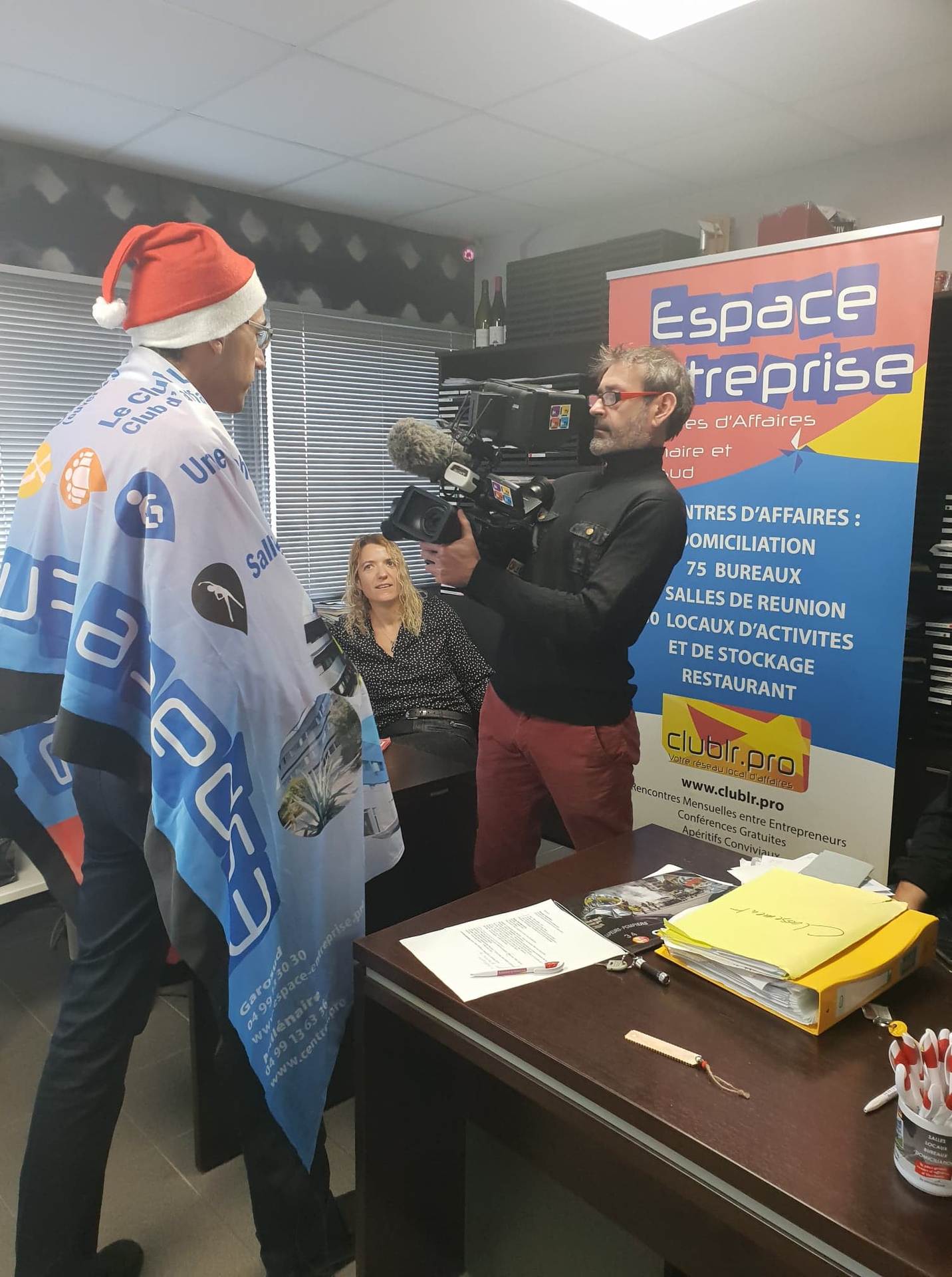 Vœux 2019 Espace Entreprise à Montpellier : membre de l'équipe en bonnet de Père Noël enroulé dans la banderole Espace Entreprise / Club LR, filmé par le cadreur.