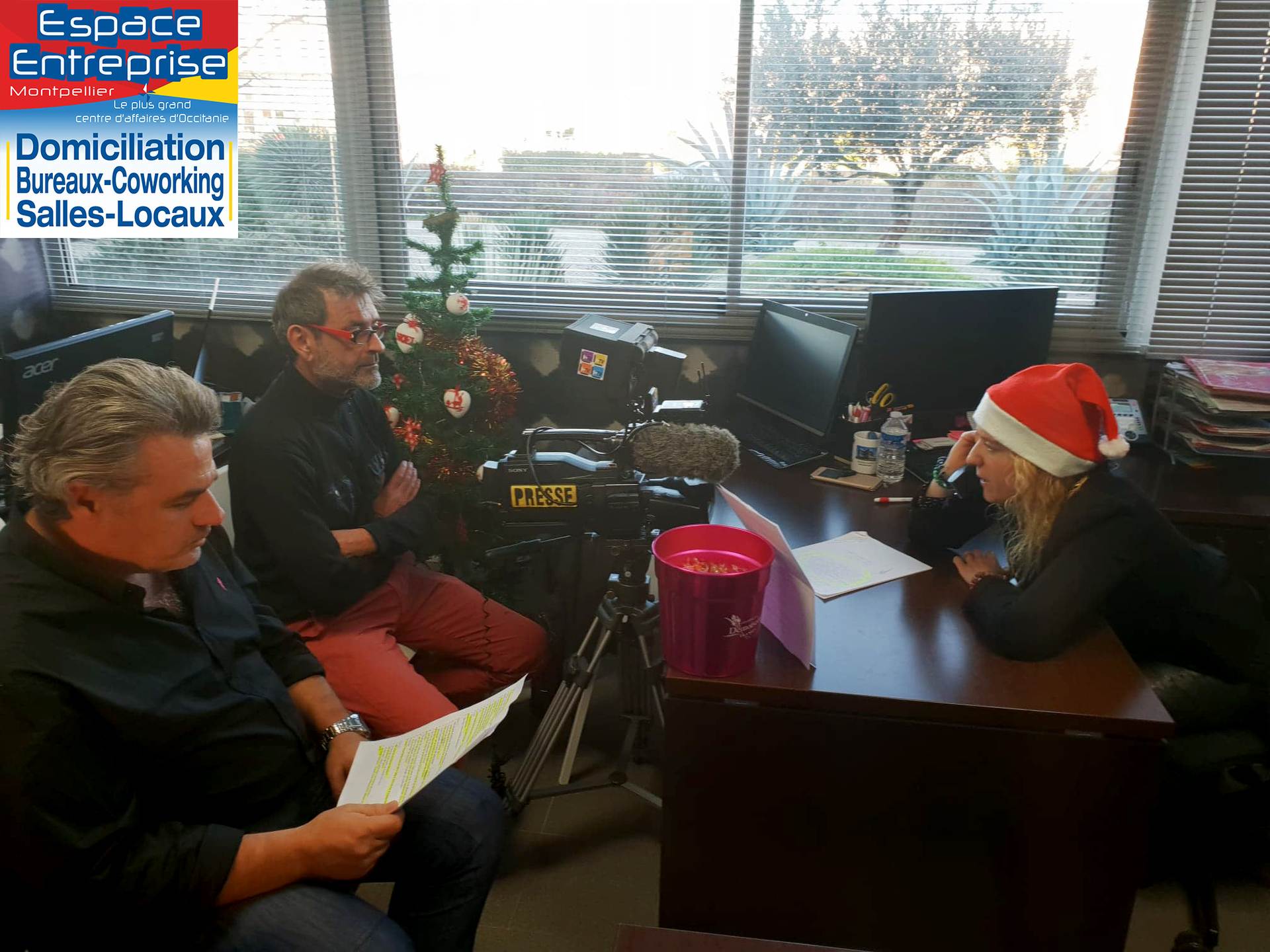 Vœux 2019 Espace Entreprise à Montpellier : équipe de tournage filmant une collaboratrice en bonnet de Père Noël, sapin de Noël et grandes baies vitrées du bureau.