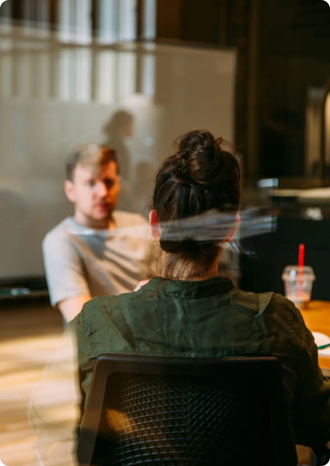 Due colleghi che conversano in ufficio, visti attraverso una parete a vetri