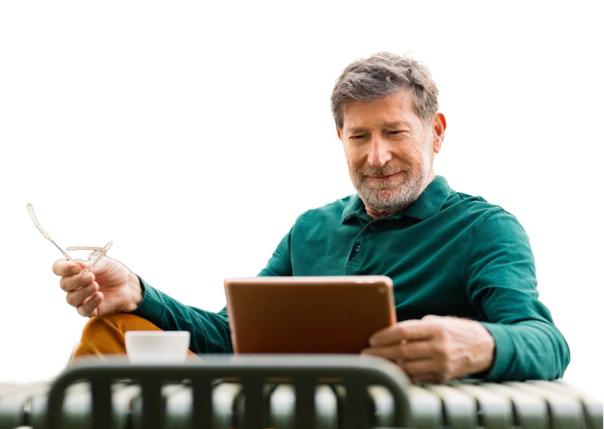 Hombre mayor sonriente leyendo en su tableta en una mesa de terraza