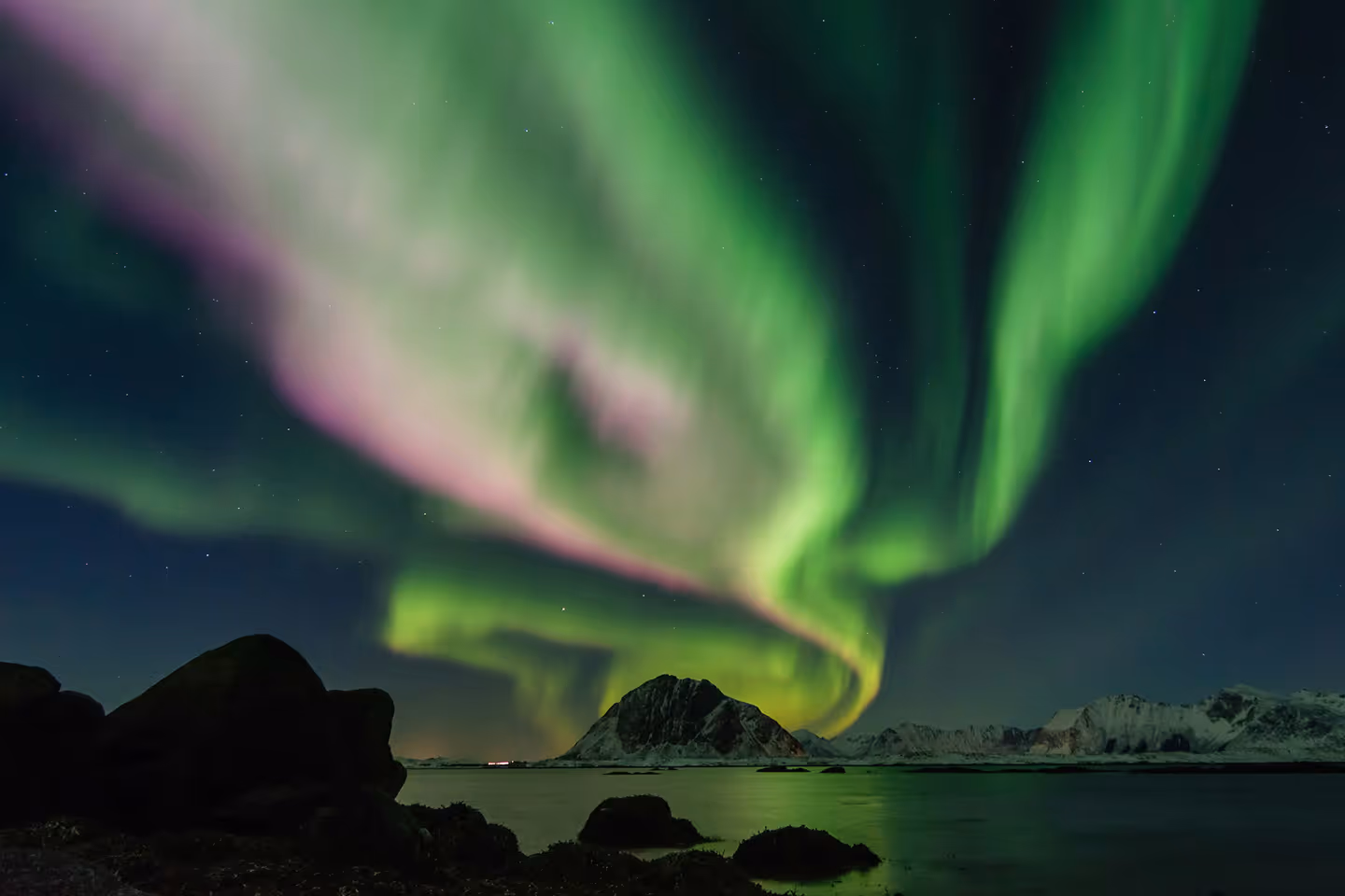 Nordlichter erhellen den Nachthimmel über schneebedeckten Bergen und einer ruhigen Wassermasse.