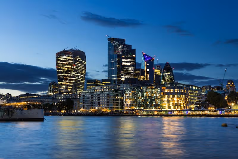 Evening view of the London skyline with illuminated skyscrapers reflecting on the River Thames.