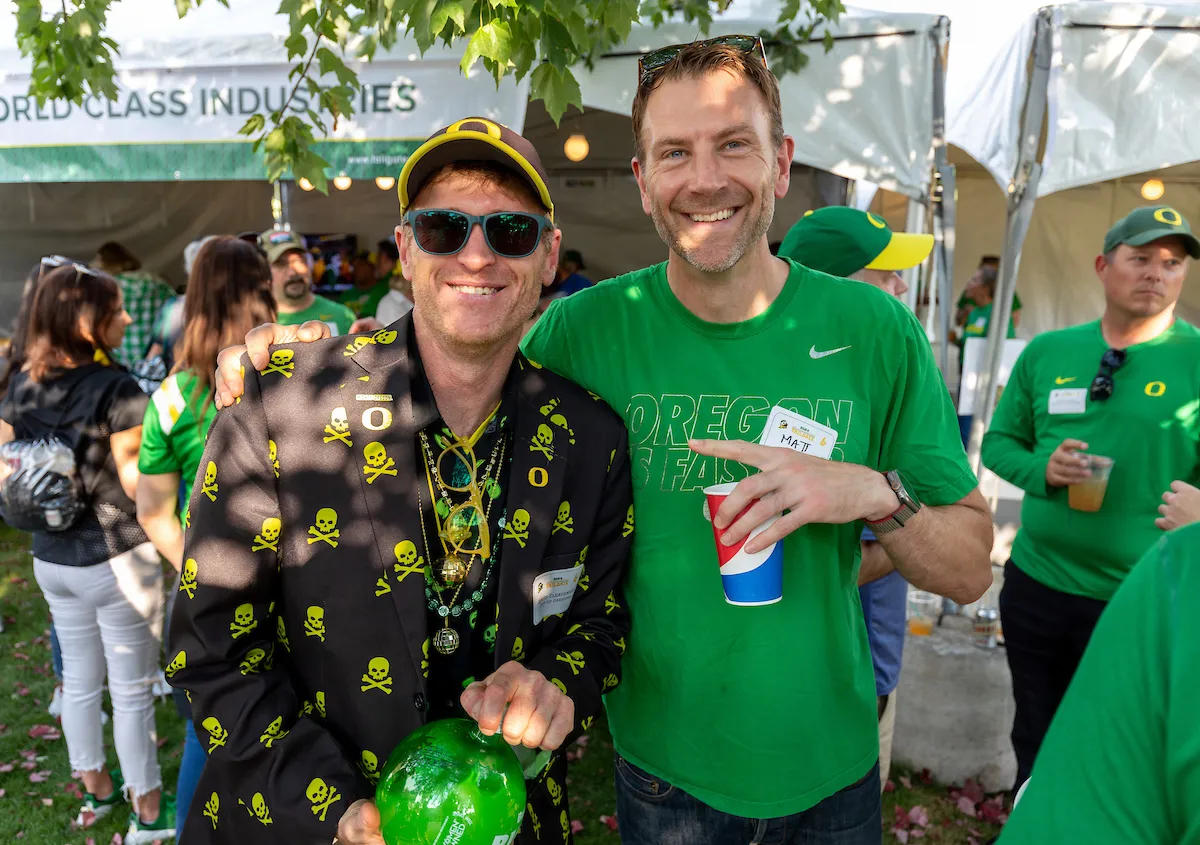 Two men wearing Ducks shirts smile together for a photo, showcasing a friendly and casual moment.
