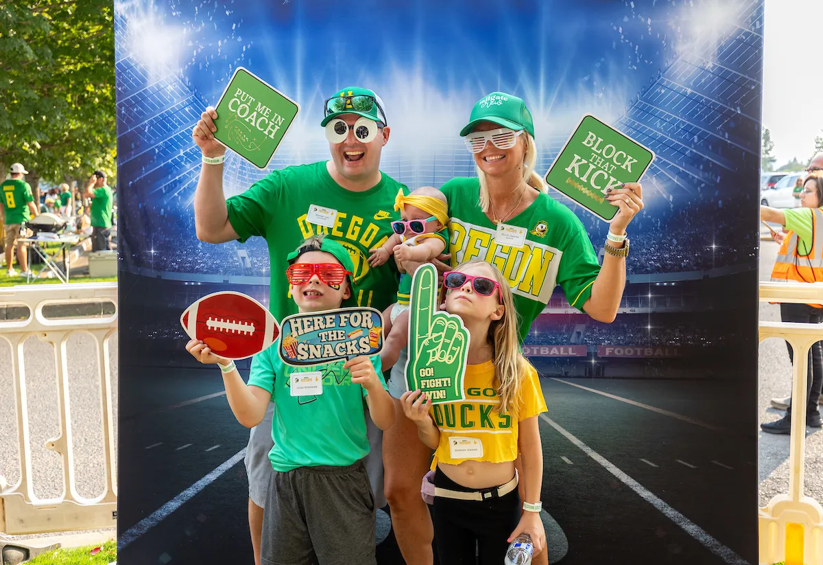 A family smiles together for a photo at a Ducks football game, capturing a moment of joy and togetherness.
