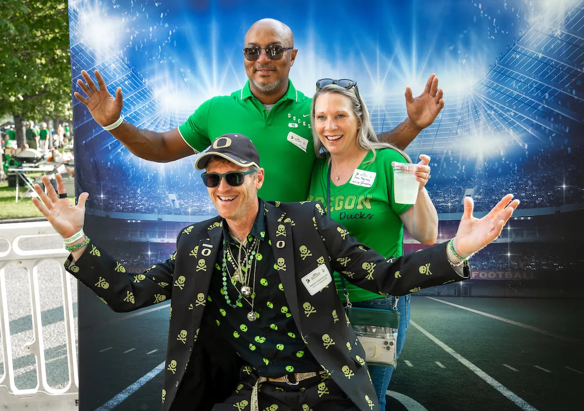 Three people wearing Oregon Ducks merch, standing together in a friendly pose.