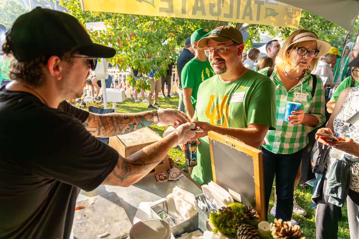 A man is offering a piece of food to another man in a casual setting.