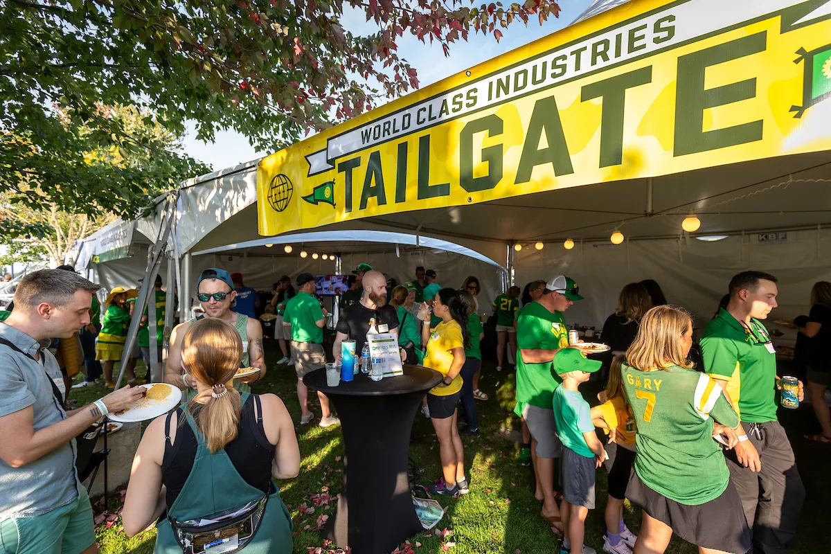A group of people gathered under a tent, smiling and standing together beneath a WCI Tailgate banner.