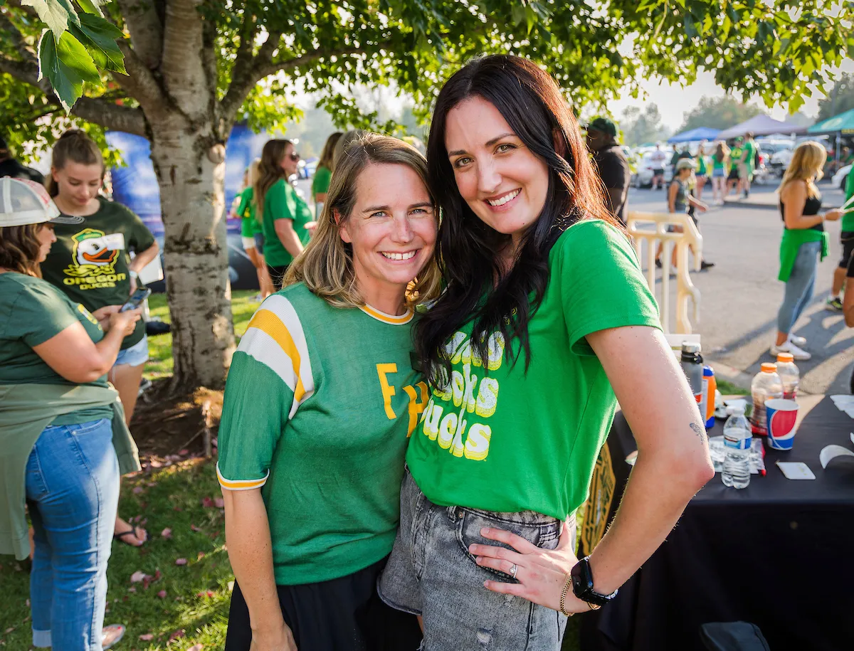 Two women wearing green shirts smiling and posing together for a photo.