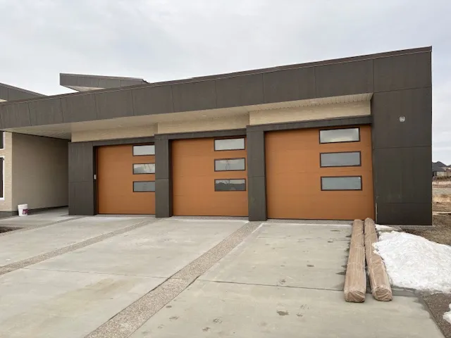 Complete Door Solutions – residential double garage doors with dark frames and stone accents.