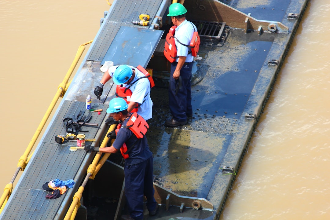 Installation process showing chains being attached to a floating dock corner, with marine construction workers in the background - floating dock tie downs Installation process showing chains being attached to a floating dock corner, with marine construction workers in the background - floating dock tie downs