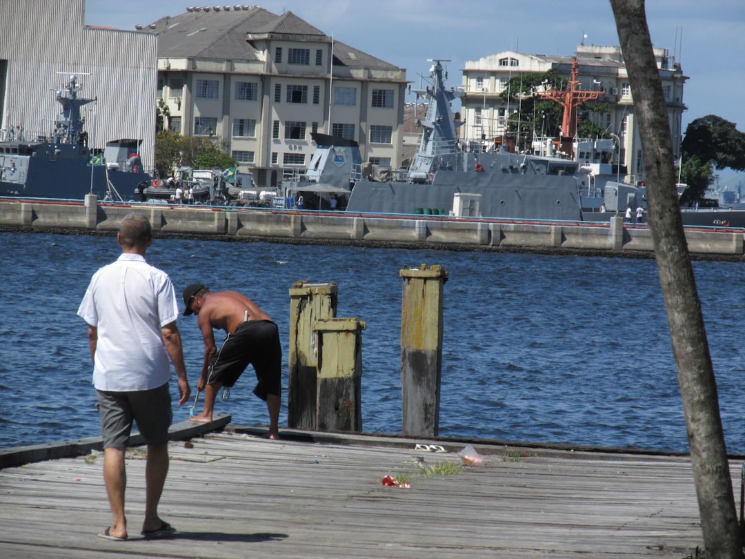 A marine contractor assesses a waterfront site, pointing towards the water, with a floating dock in the background - floating dock tie downs A marine contractor assesses a waterfront site, pointing towards the water, with a floating dock in the background - floating dock tie downs