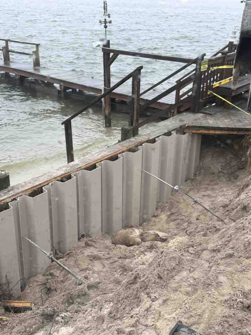 Long Island shoreline erosion threatening a waterfront home with undermined lawn and exposed roots; bright day; focus on eroding bank and failing timber bulkhead - Coastal resiliency projects Long Island shoreline erosion threatening a waterfront home with undermined lawn and exposed roots; bright day; focus on eroding bank and failing timber bulkhead - Coastal resiliency projects