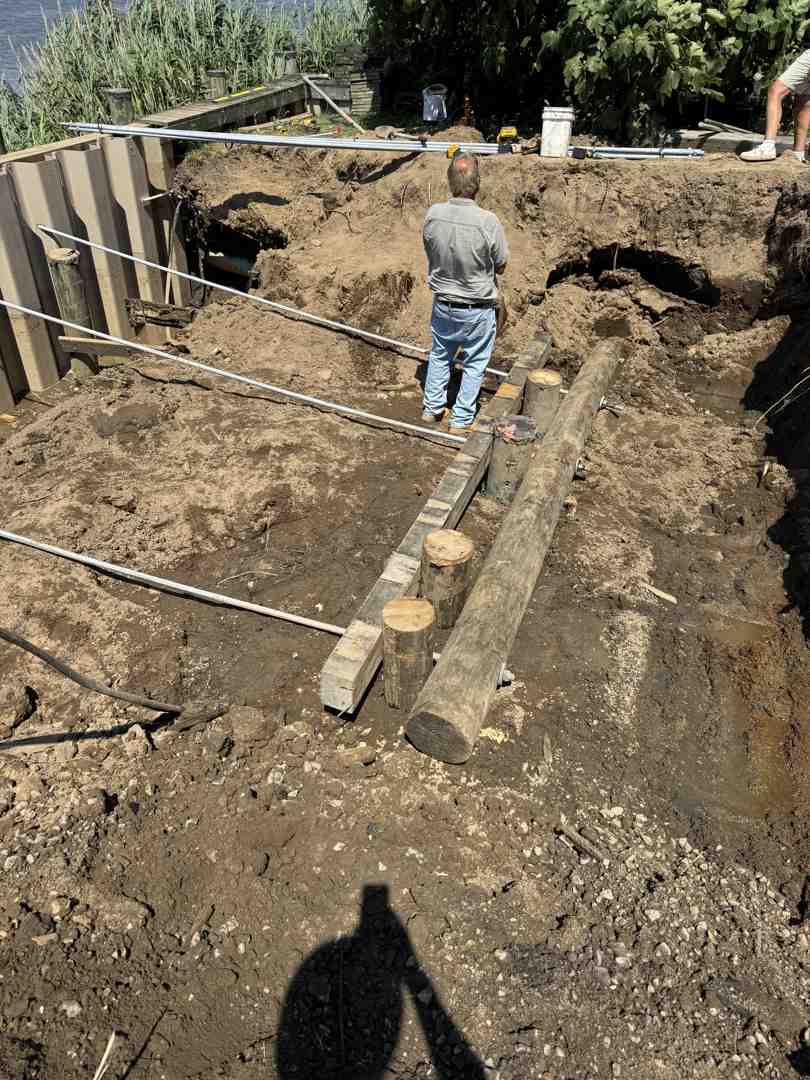 Heavy machinery excavating a deep foundation trench for a shoreline retaining wall - constructing a retaining wall with blocks Heavy machinery excavating a deep foundation trench for a shoreline retaining wall - constructing a retaining wall with blocks