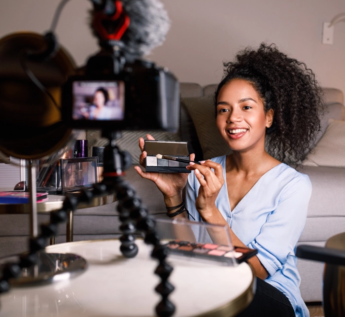 Smiling woman content creator filming makeup tutorial with professional camera and ring light in home studio
