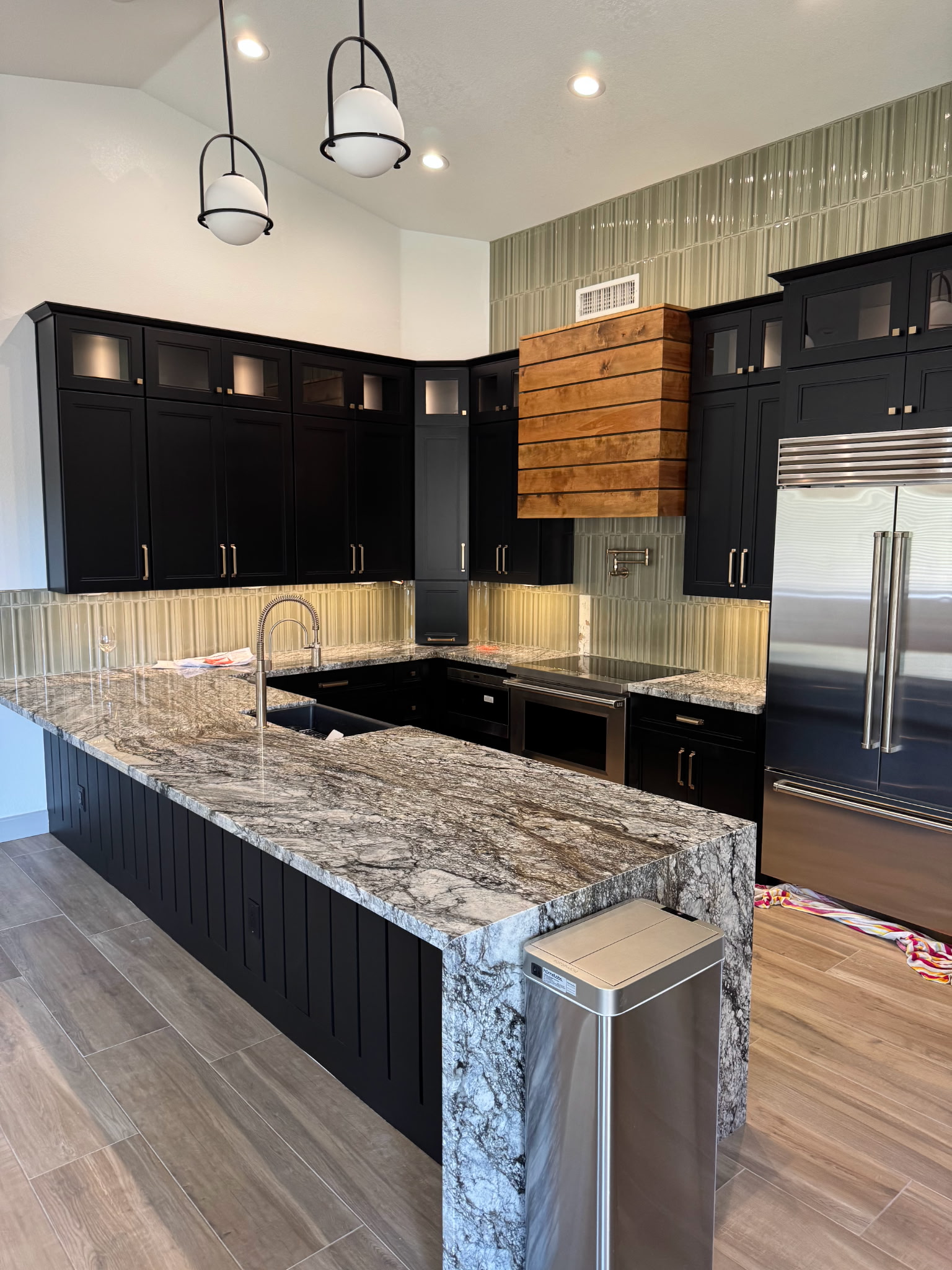 A modern kitchen remodel with a custom range hood and a waterfall granite countertop. 