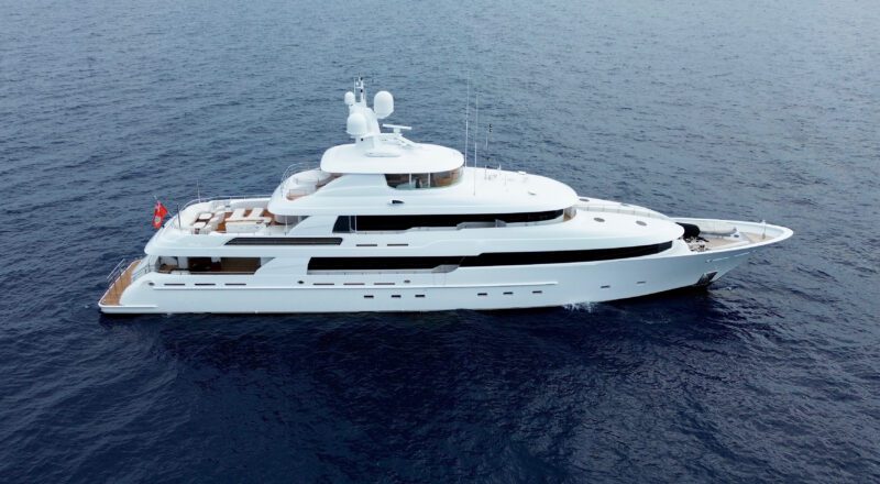 A large white Delta Marine Noverra luxury yacht cruises on calm blue ocean water, viewed from above and to the side.